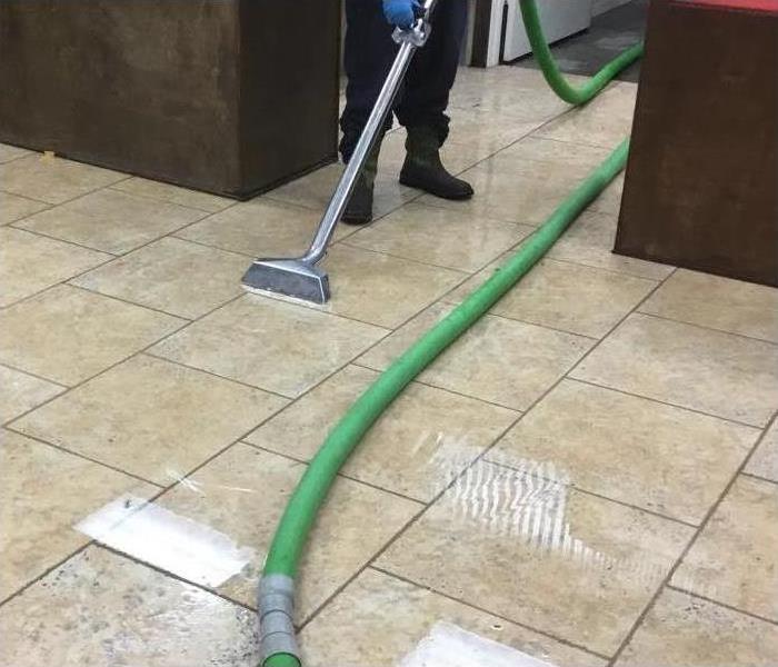 SERVPRO of Sugar Land technician cleaning standing water on tile floors with our water extraction machine.  